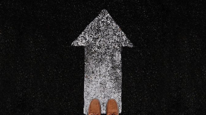 Shoes on the edge of an upward arrow painted on the floor